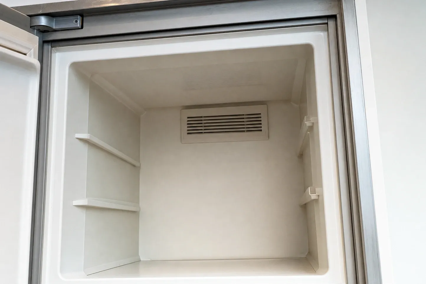 Empty freezer compartment with bare shelf ledges and the air vent grille on the rear wall